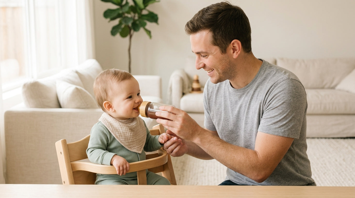A first-time dad holding a bottle of prune juice and looking confused next to his eleven month old baby.