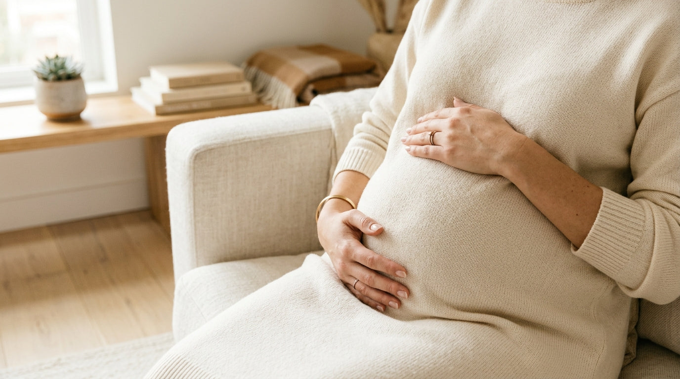 Pregnant woman holding an iced coffee looking down at her bump in confusion