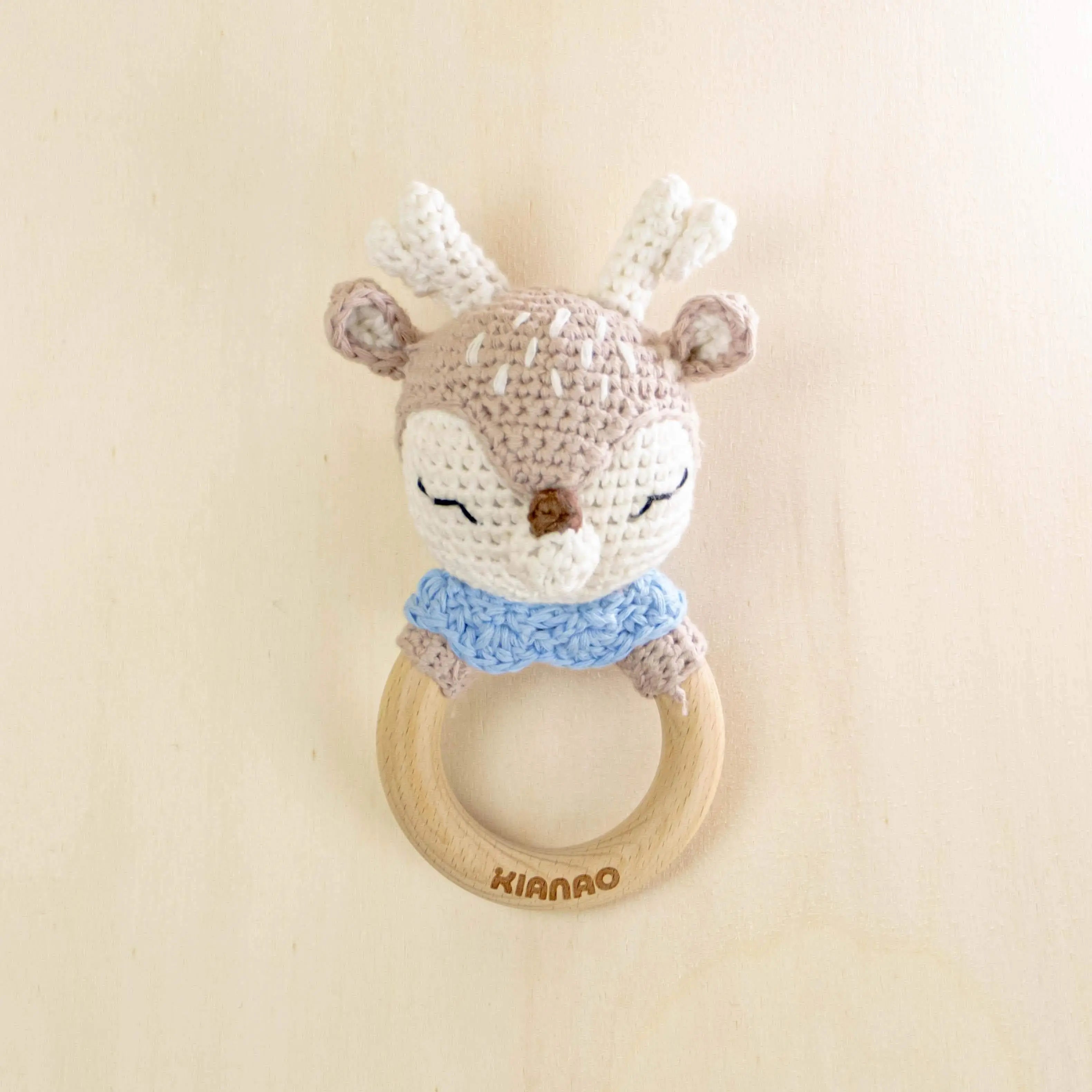 beige crochet deer rattle teething toy with blue bandana and wooden ring, organic cotton baby teether with cute antlers and sleepy expression