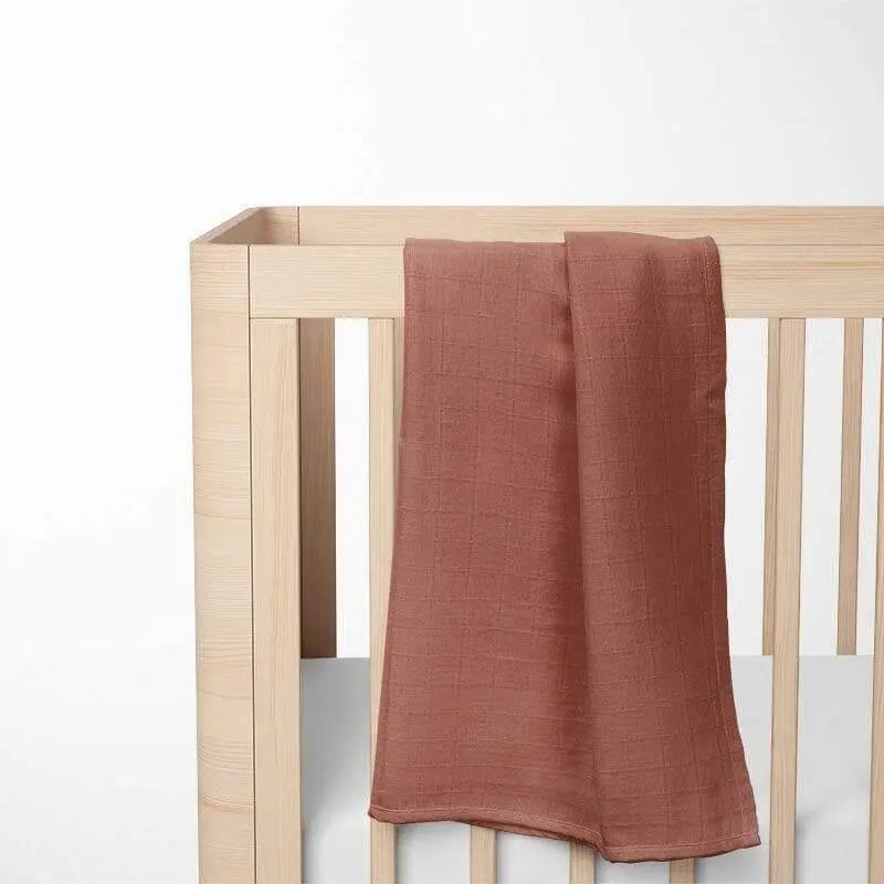 terracotta bamboo baby blanket laid out on wooden crib, showcasing the warm color and lightweight fabric