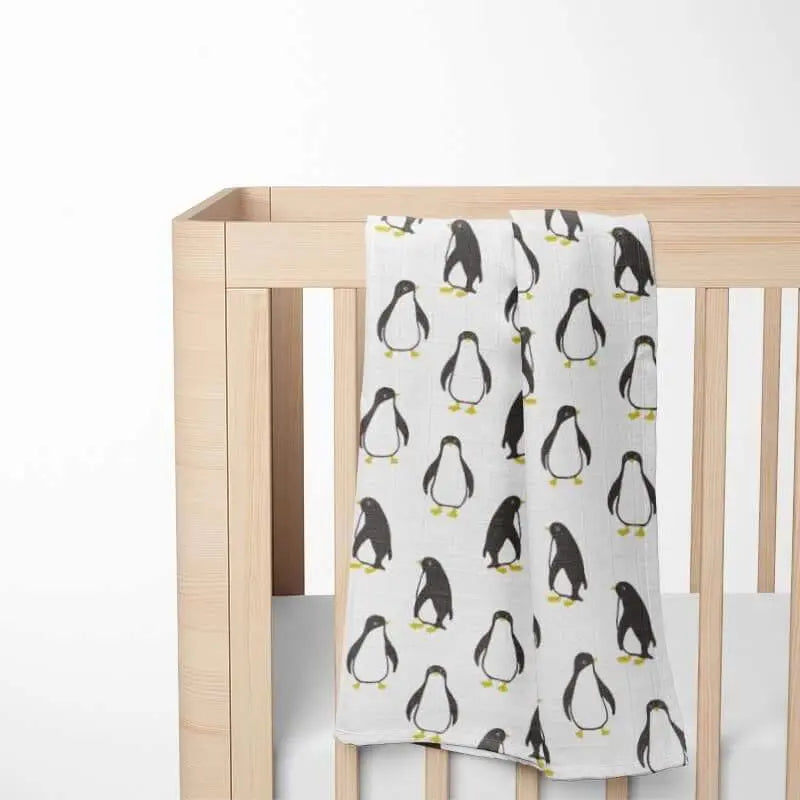 folded white baby blanket with black and yellow penguin pattern displayed on wooden crib showing double-layer organic cotton construction