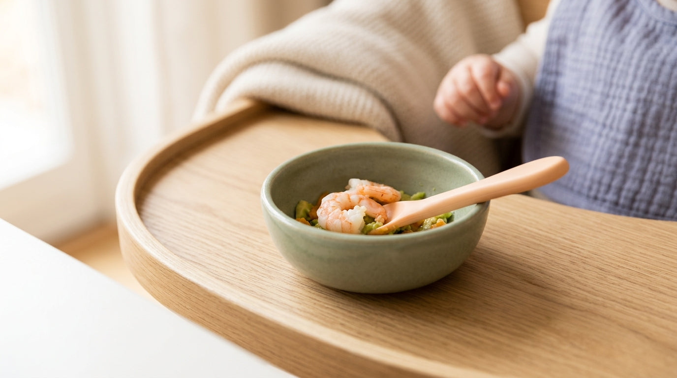 A messy baby wearing a bib while eating pureed shrimp and avocado mix.