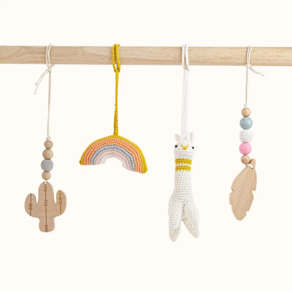 Close-up of Alpaca Play Gym featuring white crocheted alpaca, colorful rainbow, wooden cactus and beaded cloud toys