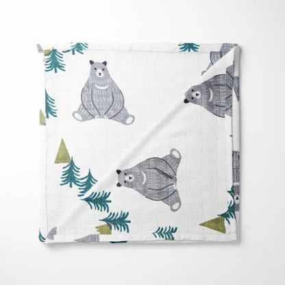 folded bamboo baby blanket featuring woodland bears, pine trees and triangular mountains on white background with soft grid texture
