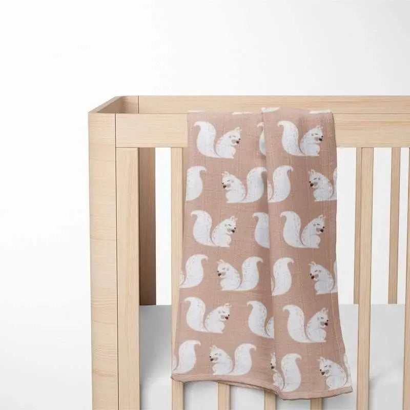 beige organic cotton baby blanket with squirrel pattern displayed in wooden crib showing perfect size and nursery integration