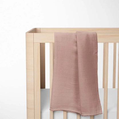 brick red bamboo baby blanket laid out on wooden crib, highlighting the sunny color and lightweight breathable design