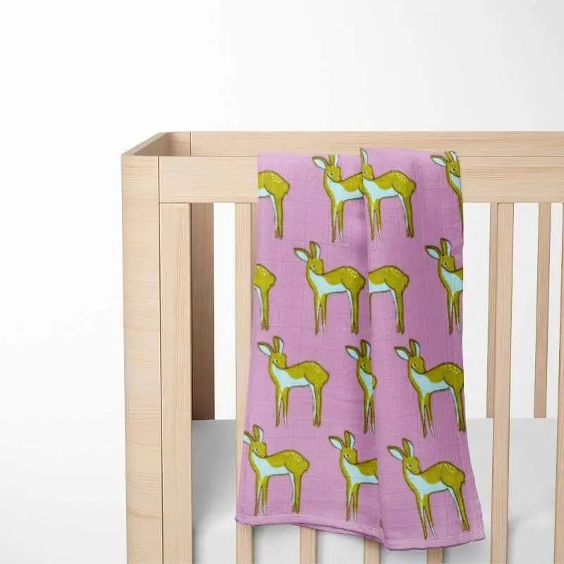 folded purple baby blanket with green deer pattern displayed on wooden crib showing double-layer organic cotton construction