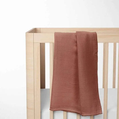 terracotta bamboo baby blanket laid out on wooden crib, showcasing the warm color and lightweight fabric