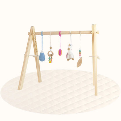 Side view of wooden Unicorn Play Gym showing A-frame design with hanging crochet toys on cream playmat
