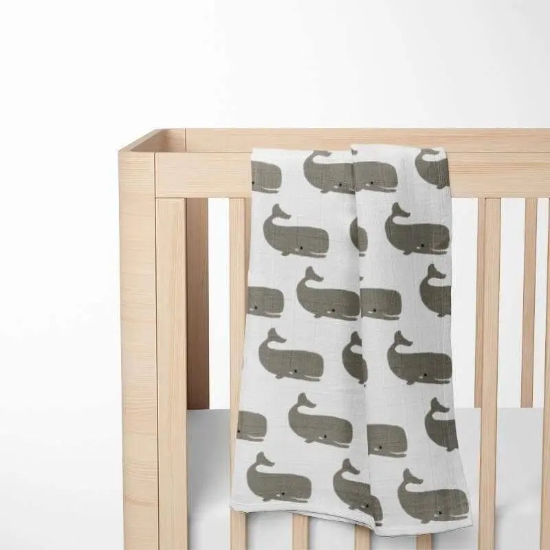 folded white baby blanket with gray whale pattern displayed on wooden crib showing double-layer organic cotton construction