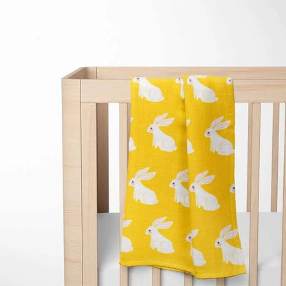 yellow organic cotton baby blanket with bunny pattern displayed in wooden crib showing size and nursery integration