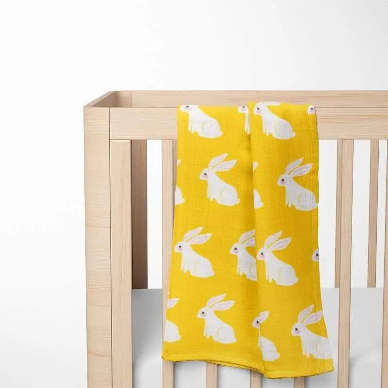 yellow organic cotton baby blanket with bunny pattern displayed in wooden crib showing size and nursery integration